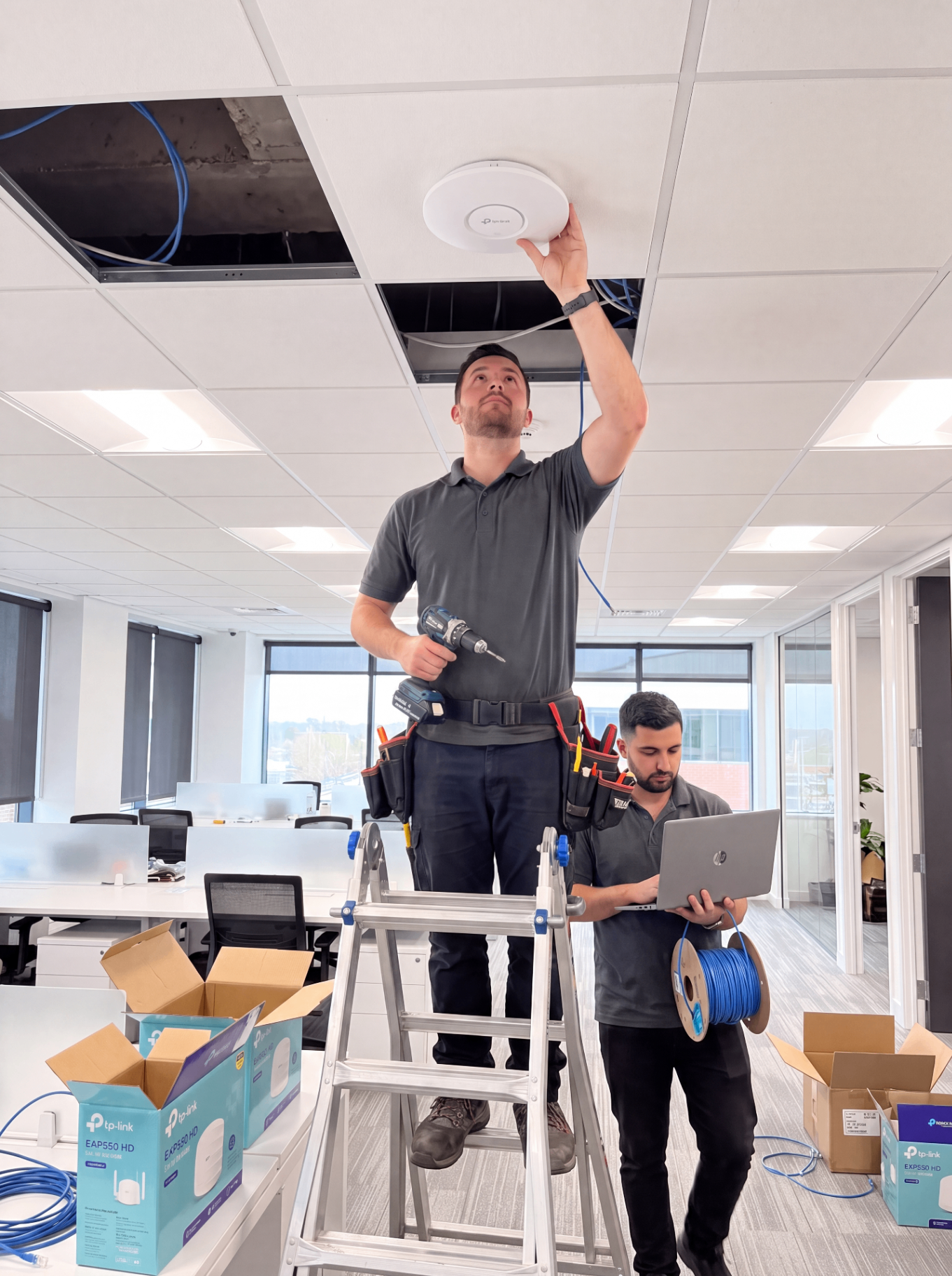 Two technicians installing a ceiling device with a laptop and cable